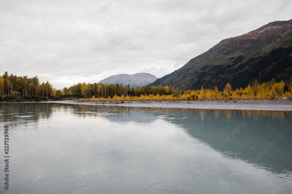 Fall colors reflecting in a calm glacial river on a cloudy day