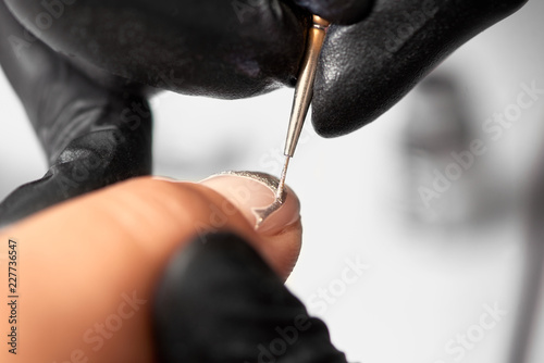 Close-up of professional manicurist hands in black rubber gloves painting elegant abstract silver glitter pattern on client woman painted nails using thin applicator brush in beauty salon.