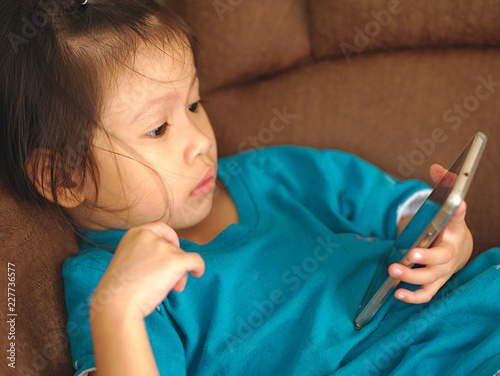 Wallpaper Mural Little Asian kid using smartphone on sofa bed. Torontodigital.ca