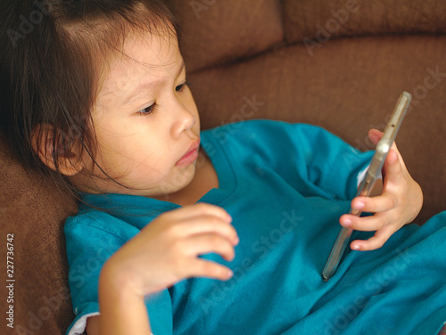 Little Asian kid using smartphone on sofa bed.