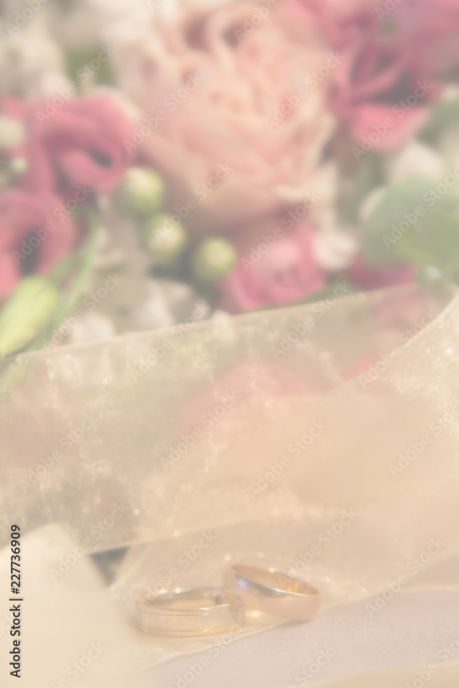 Fototapeta premium Wedding blurred background: wedding rings near the natural roses bouquet vertical