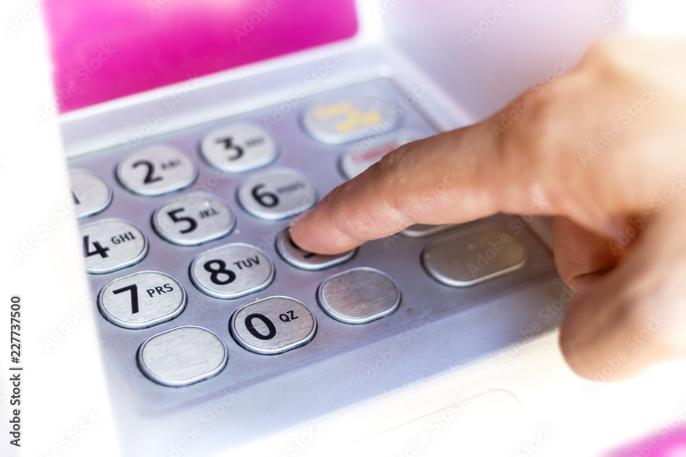 Close up of hand entering pin at an ATM. Finger about to press a pin code on a pad. Security code on an Automated Teller Machine.