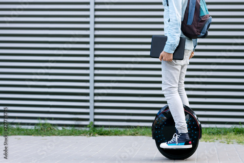 Modern young adult male businessman student freelancer with backpack and laptop riding on ecological electric transport futuristic eco electric unicycle scooter, balancing electric wheel. Eco planet. photo