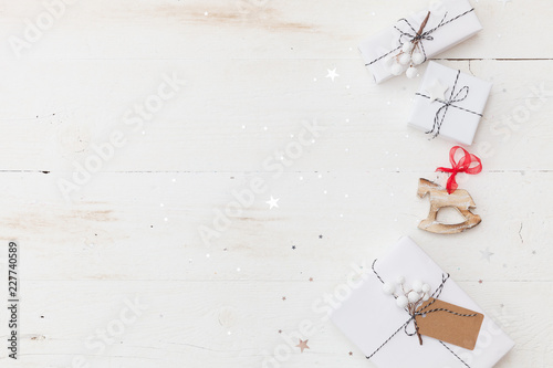 Obraz na plátně Top view on nice Christmas gifts wrapped in white gift paper, Christmas tree decorations on white wooden background with sparkling stars