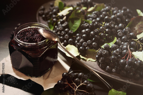 Jam from black chokeberries   Aronia melanocarpa   and its berries on dark table. Homemade preserves. Horizontal.