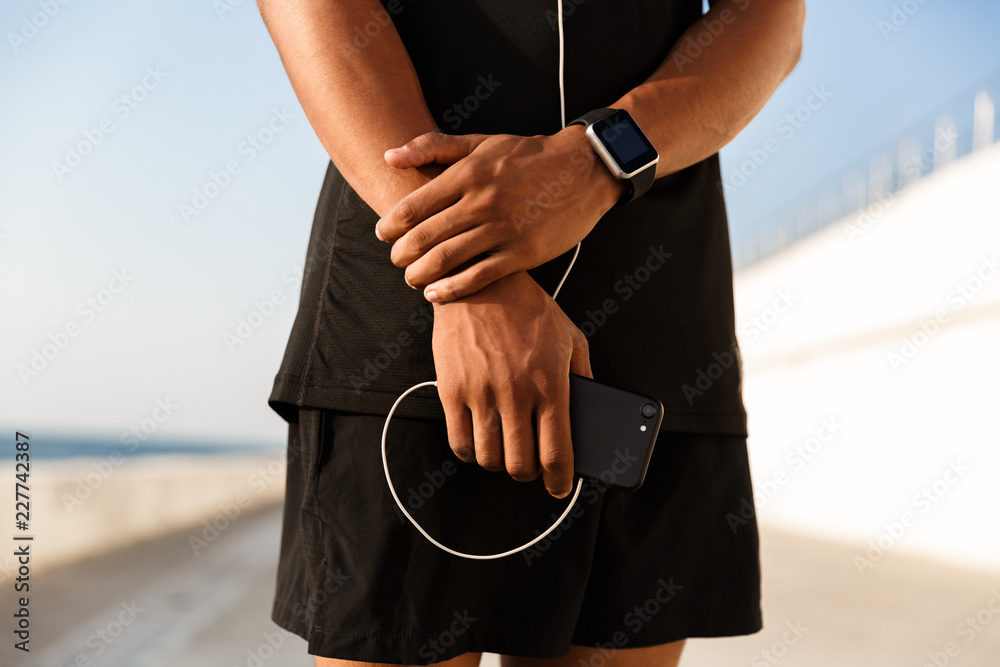 Guy sportsman outdoors on the beach holding phone and earphones.