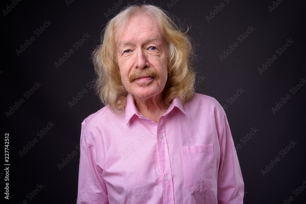 Senior businessman wearing pink shirt against gray background Senior businessman wearing pink shirt against gray background