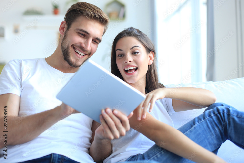 Young couple watching media content online in a tablet sitting on a sofa in the living room. Young couple watching media content online in a tablet sitting on a sofa in the living room.