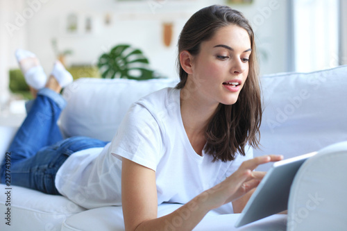 Beautiful young woman using tablet sitting on sofa at home at living room.