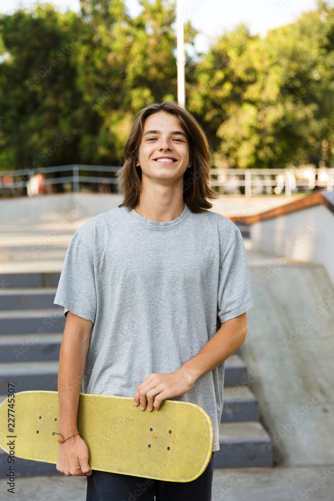 Photo of teenager 16-18 in casual wear standing with skateboard in skate park, during summer day Stock Photo | Adobe Stock