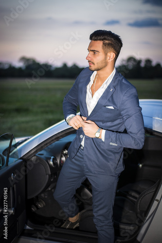 Portrait of young attractiave man in business suit sitting in his new stylish car outdoor in countryside photo