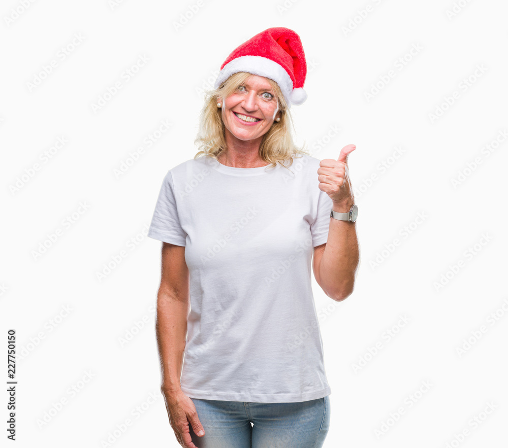 Middle age blonde woman wearing christmas hat over isolated background doing happy thumbs up gesture with hand. Approving expression looking at the camera with showing success. Middle age blonde woman wearing christmas hat over isolated background doing happy thumbs up gesture with hand. Approving expression looking at the camera with showing success.