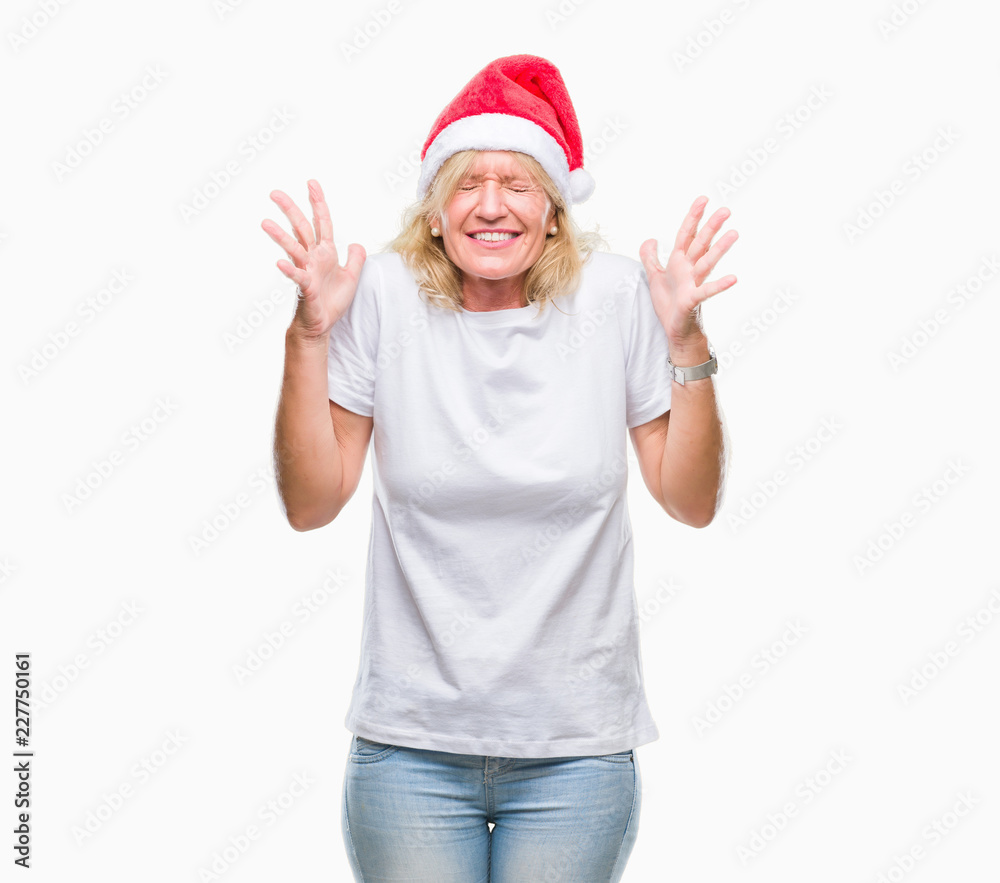 Middle age blonde woman wearing christmas hat over isolated background celebrating mad and crazy for success with arms raised and closed eyes screaming excited. Winner concept Middle age blonde woman wearing christmas hat over isolated background celebrating mad and crazy for success with arms raised and closed eyes screaming excited. Winner concept