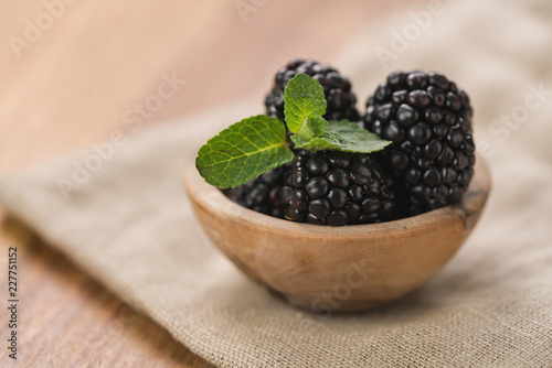 fresh blackberries in wood bowl on wooden table with mint leaves