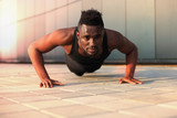 African man in sports clothing keeping plank position while exercising outdoors.