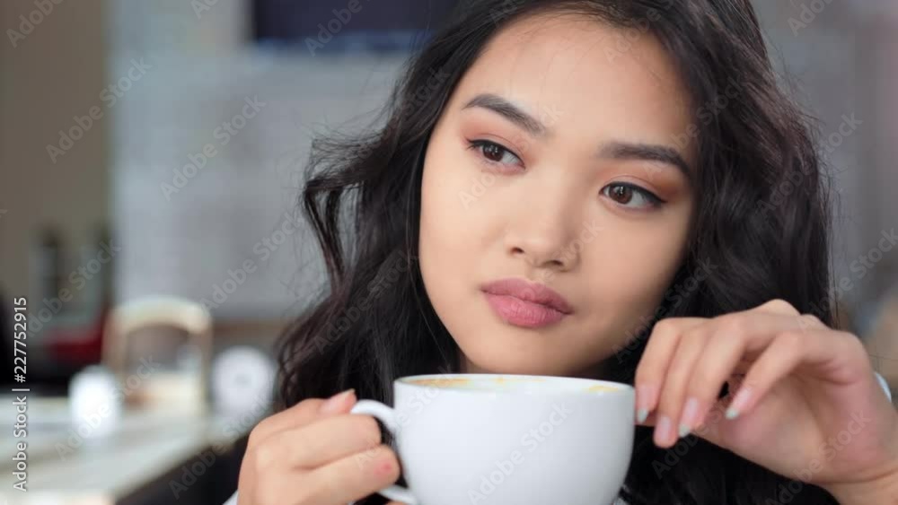 Pensive beautiful Asian young woman thinking and enjoying drinking coffee close-up portrait Pensive beautiful Asian young woman thinking and enjoying drinking coffee close-up portrait