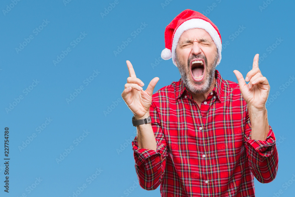 Naklejka premium Middle age hoary senior man wearing christmas hat over isolated background celebrating mad and crazy for success with arms raised and closed eyes screaming excited. Winner concept