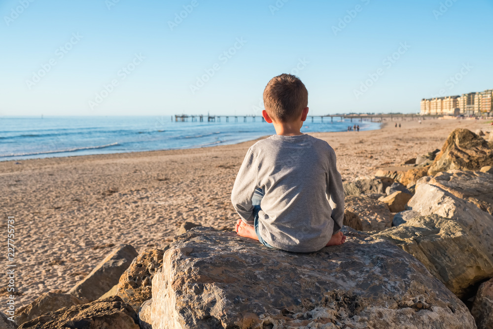 Lonely barefoot boy sitting on the rock