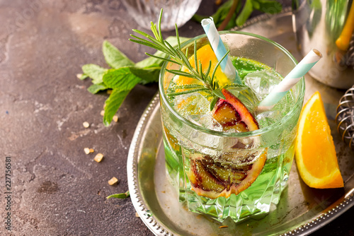 Sweet refreshing mint liqueur, with ice, red mandarin and rosemary on the metal tray to feed on gray concrete stone table,