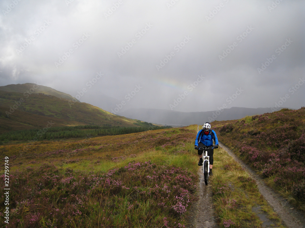 Cyclist on a bridleway in Torridon, Scottish Highlands, as rain pours from the sky and distant hills are shrouded in cloud