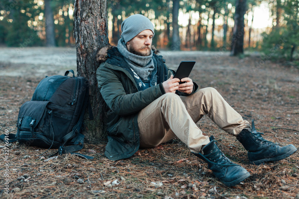 adult handsome Male traveler Sits On autumn pine forest Near tree, Holding At Tablet Recreation Resting Travel Destination Concept adult handsome Male traveler Sits On autumn pine forest Near tree, Holding At Tablet Recreation Resting Travel Destination Concept