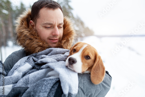 A young man wrapped his best friend Beagle dog in a warm blanket to warm him in a cold snowy winter.