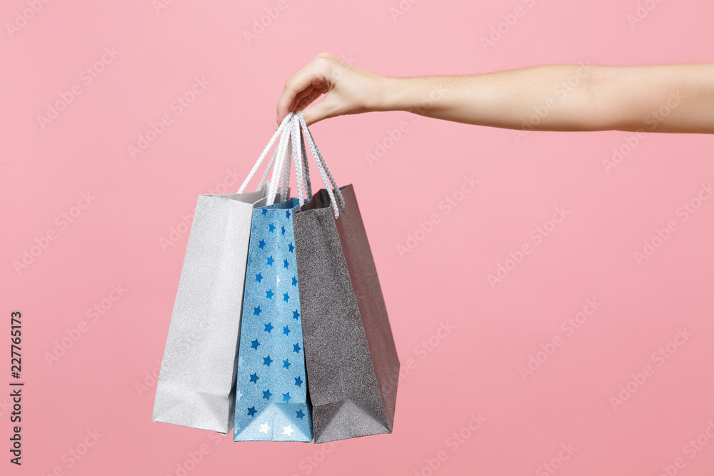 Close up female holds three colored clear empty blank craft paper gift bag for purchases after shopping isolated on pastel pink background. Packaging template mockup. Delivery concept advertising area