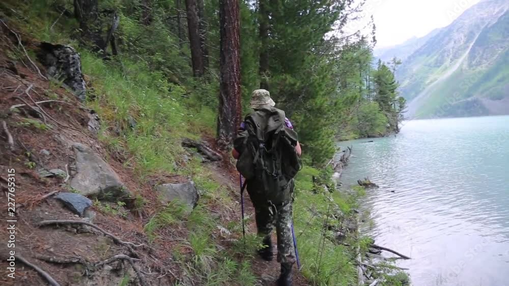 A man with a backpack walks along a mountain river. A tourist with a large bag on his back walks along the rocks near a noisy fast river. A man with a backpack walks along a mountain river. A tourist with a large bag on his back walks along the rocks near a noisy fast river.
