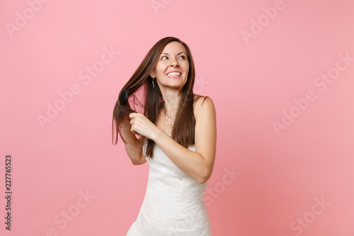 Portrait of smiling joyful bride woman in beautiful white wedding dress holding comb, combing her hair isolated on pastel pink background. Wedding celebration concept. Copy space for advertisement.