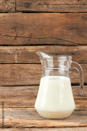 Organic milk in glass jug. Natural cow milk in glass pitcher on rustic wooden boards. Health benefits of milk.