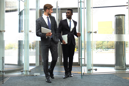 Fotografija Two multinational young businessmen entering in office building with glass doors