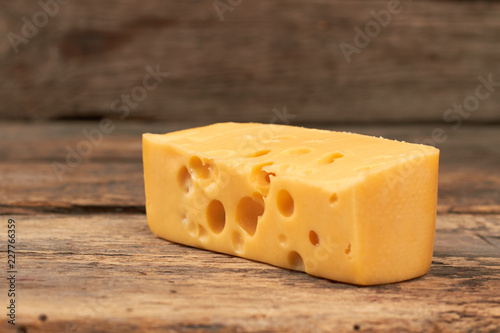 Piece of maasdam cheese on wooden background. Yellow cheese with holes on rustic wooden boards. Healthy milky product.