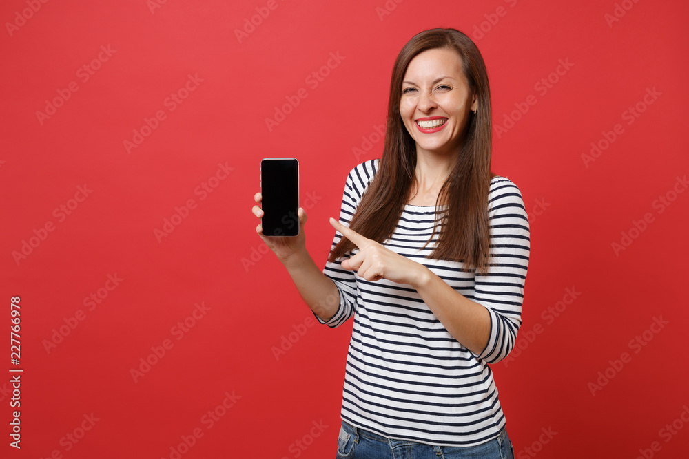 Portrait Of Pretty Young Woman Pointing Index Finger On Mobile Phone With Blank Black Empty Screen Isolated On Bright Red Background People Sincere Emotions Lifestyle Concept Mock Up Copy Space Stock Photo