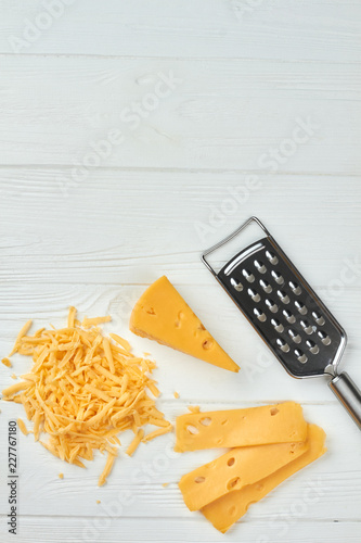 Emmental cheese on white wooden background. Fresh Swiss cheese, grater and copy space, vertical image.