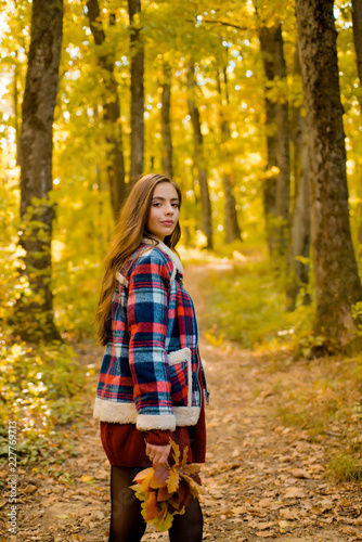 Autumn sale. Beautiful happy smiling girl with long hair wearing stylish jacket posing in autumn day. Autumn portrait smiling woman holds yellow maple leaves in park. © Volodymyr