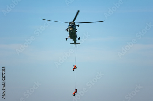 Rescue helicopter and rescuer on the rope - life-saving flying vehicle and blue sky (muted contrast)