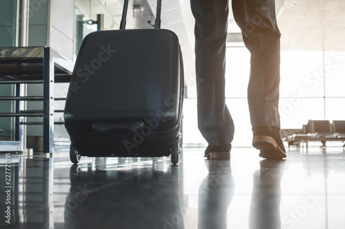 Businessman carrying suitcase on wheels and moving forward. Focus on baggage