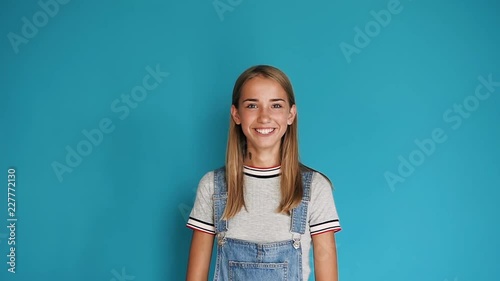 Happy smiling caucasian young girl. Portrait of cute teen girl with long hair smiling at the camera on blue background. Close up, portrait of attractive girl smiling confident and pretty