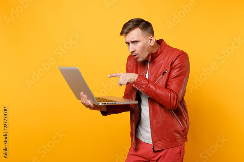 Portrait vogue fun handsome young man in red leather jacket, t-shirt using laptop pc tablet isolated on bright trending yellow background. People sincere emotions lifestyle concept. Advertising area.