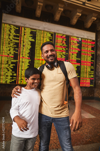 International travelers. Joyful smiling hindu boy and his father standing near departure arrival board while expressing joy
