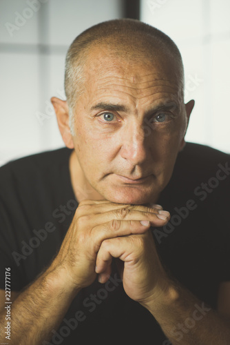 A man is posing in studio with clasped hands under the chin, looking at the camera. photo