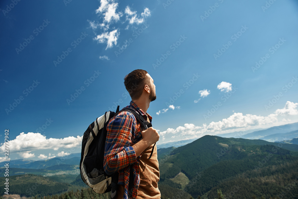 Naklejka premium Man carrying backpack during tour in highland. He is standing on top and watching downhill