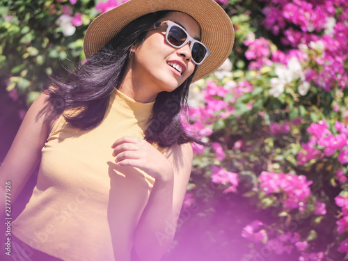 Happy Asian woman wearing hat and sunglassses with pink bokeh background in sunny day.