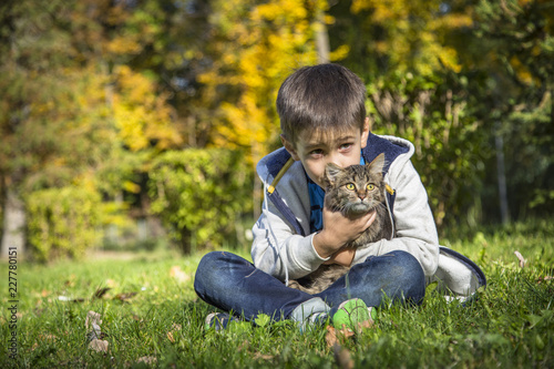 Happy little boy in the autumn park with pet kitten.