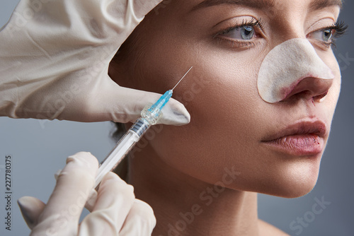 Young lady looking serious while professional doctor touching her face and making necessary injection