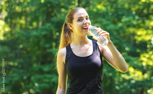 Young woman with a water bottle on a bright summer day in the forest