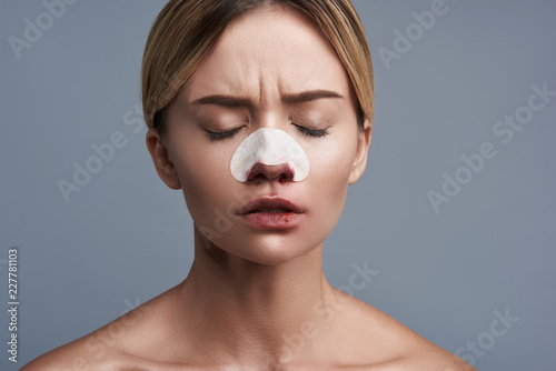 Upset serious woman closing her eyes while having bloody nose with strip on it