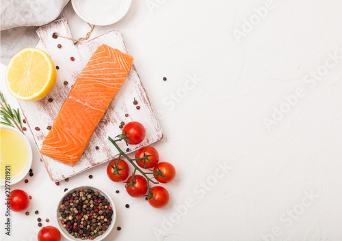Fototapeta Naklejka Na Ścianę i Meble -  Fresh raw salmon slice on chopping board with oil tomatoes and lemon on stone kitchen table background. Space for text. With rosemary and salt