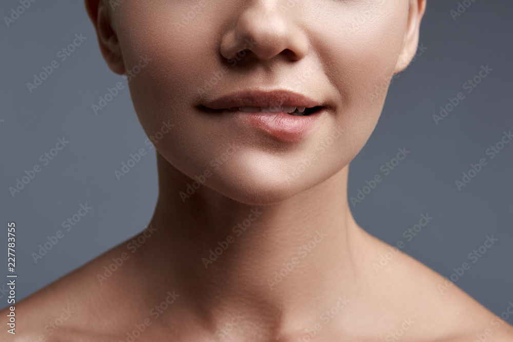 Fototapeta premium Gryzące usta. Portret na szarym tle curios kobieta gryzie jej wargi podczas myślenia
