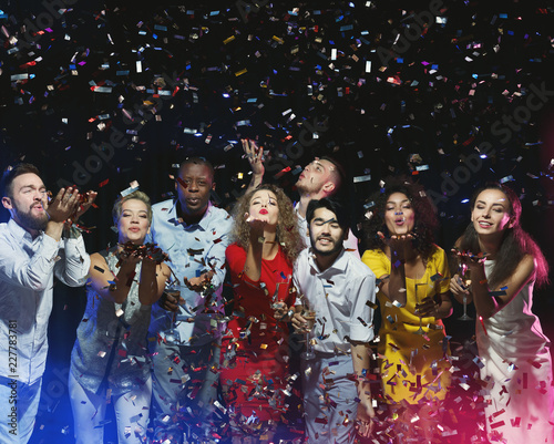 Group of friends enjoying party and blowing confetti